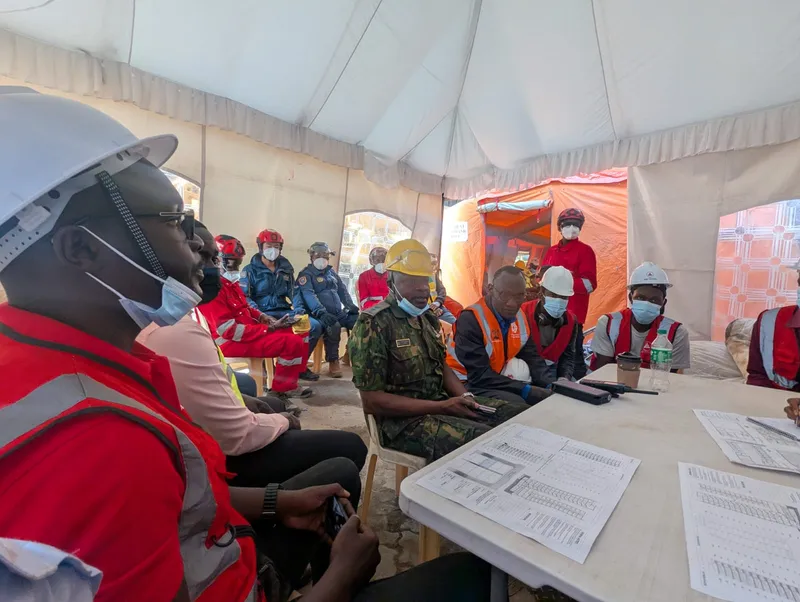 A briefing in the tent during the site visit: AAK's team, responders in red and an officer in uniform around a table of printed sheets